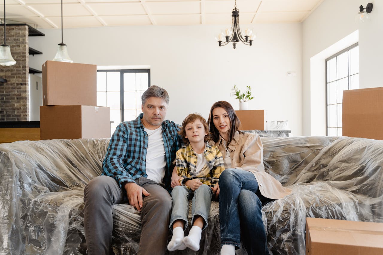 A family sitting on a covered sofa in their new home surrounded by moving boxes.